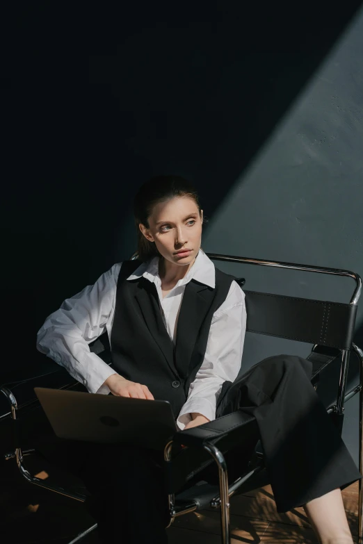 a woman sitting in a chair with a laptop, inspired by Marina Abramović, trending on pexels, renaissance, portrait androgynous girl, lawyer clothing, wearing a vest, pale skin