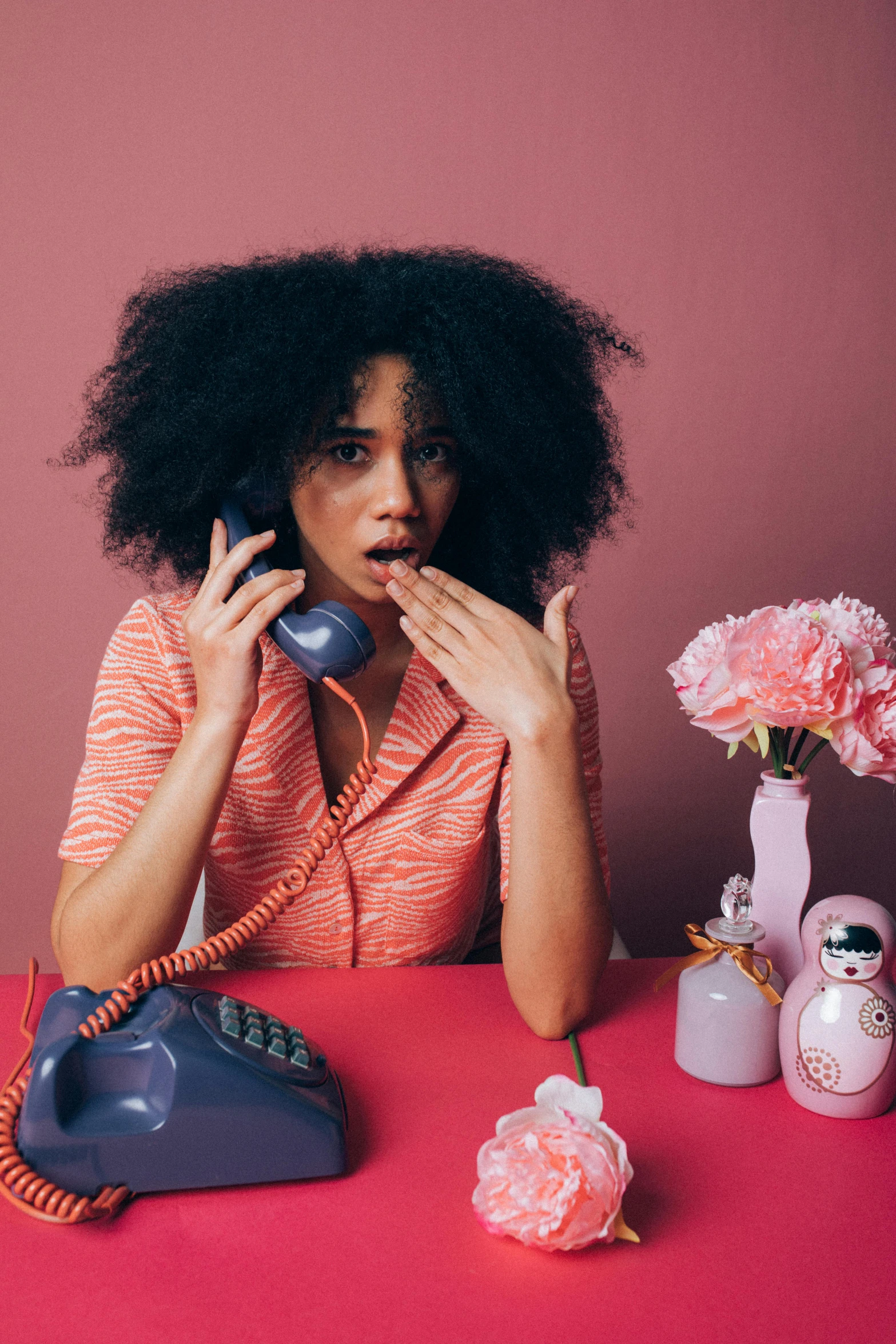 a woman sitting at a table talking on a phone, trending on pexels, magic realism, black curly hair, ((pink)), worried, retro colour