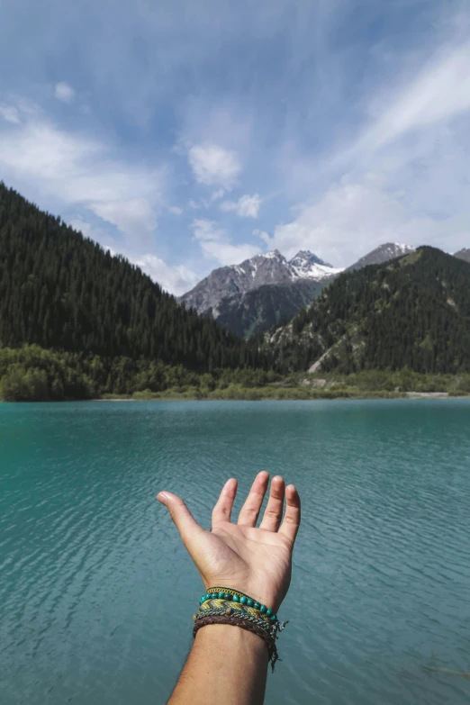 a close up of a person's hand near a body of water, mountain, turqouise, artem chebokha, whistler