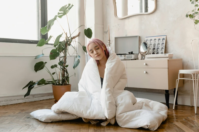 a woman sitting on the floor in a white robe, inspired by Elsa Bleda, pexels contest winner, sleeping bag, in a japanese apartment, quilt, product introduction photo