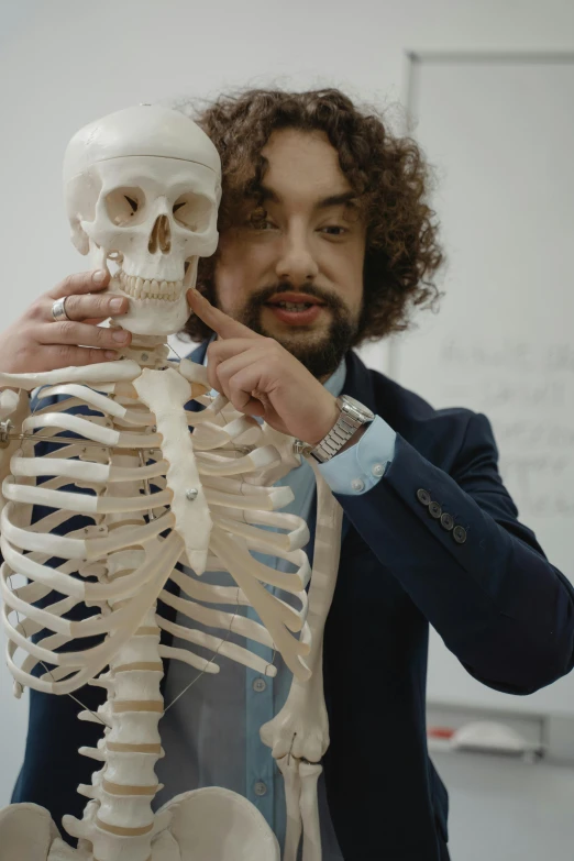 a man holding a model of a human skeleton, inspired by Germán Londoño, featured on reddit, academic art, peter dinklage, still from a music video, zack de la rocha, professor calculus