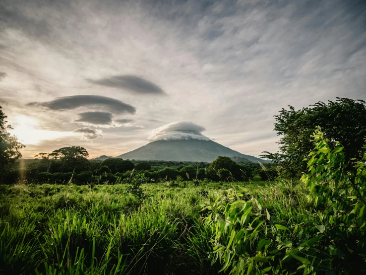 a lush green field with a mountain in the background, by Alison Geissler, unsplash contest winner, sumatraism, infographic of active volcanoes, giant cumulonimbus cloud, landscape of africa, thumbnail