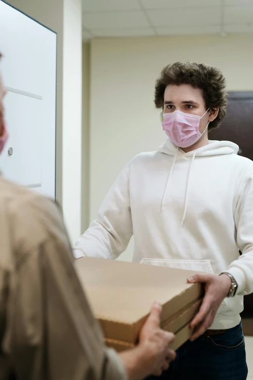 a man wearing a face mask holding a box, a stock photo, by Everett Warner, shutterstock, timothee chalamet, pathology, welcoming, person in foreground