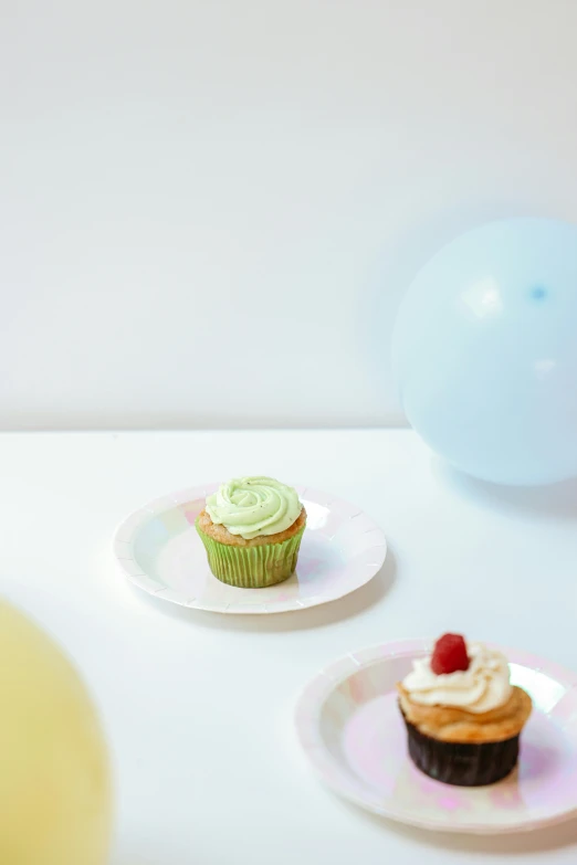 a couple of plates that have cupcakes on them, party balloons, pastel colours overlap, day light, profile image