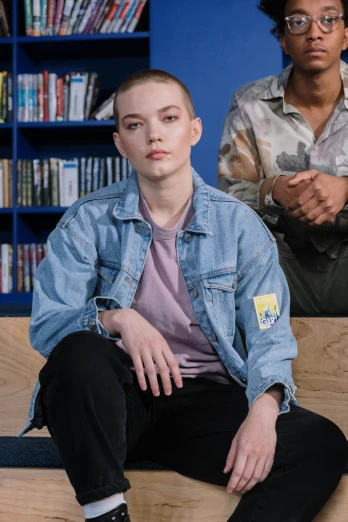 two people sitting on a bench in front of a bookshelf, a portrait, by Eve Ryder, antipodeans, wearing a jeans jackets, anya taylor-joy, shaved head, official store photo
