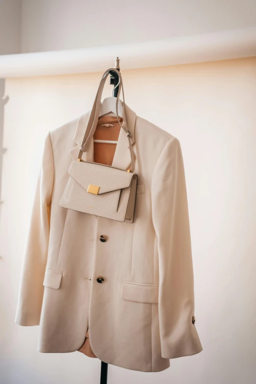 a coat hanging on a hanger in a room, by Nina Hamnett, trending on pexels, wearing white suit, holding a leather purse, uniform off - white sky, wedding