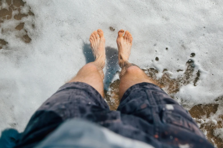 a person standing on top of a beach next to the ocean, pexels contest winner, wet feet in water, snow on the body, wearing shorts and t shirt, unshaven