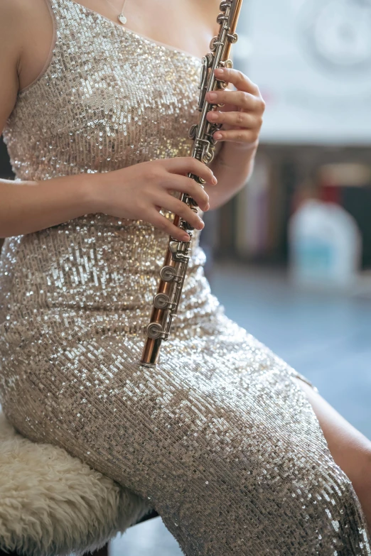 a woman sitting on a chair holding a flute, trending on pexels, arabesque, wearing a sparkling dress, small in size, low detail, sequins