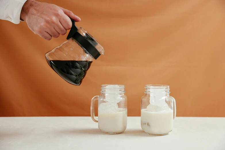 a person pouring milk into two mason jars, black, product view, aussie baristas, sandman