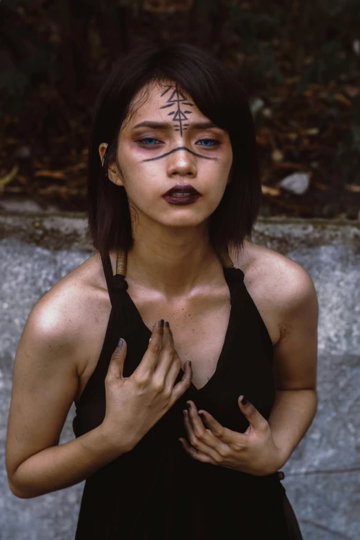a woman in a black dress posing for a picture, inspired by Taro Yamamoto, unsplash, aestheticism, facial tribal markings, set on singaporean aesthetic, postapocalyptic vibes, black eyed