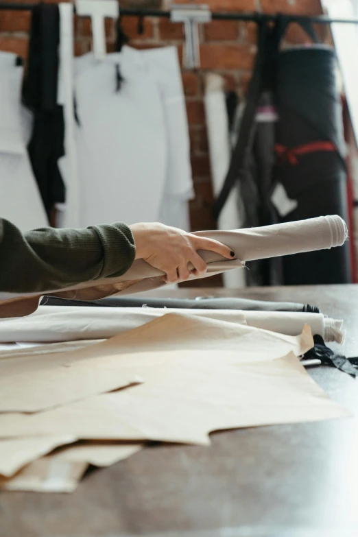 a man sitting at a table working on a piece of paper, clothing design, holding a baguette, promo image, cotton fabric