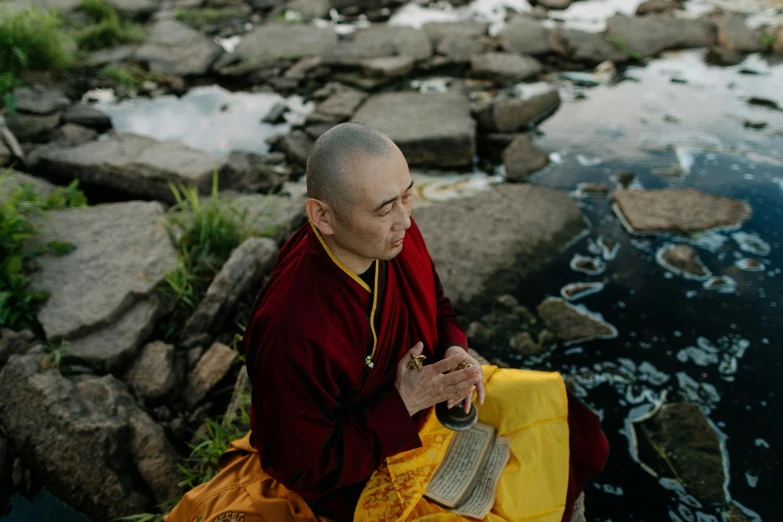 a monk sitting next to a body of water, a portrait, unsplash, with yellow cloths, wearing red robes, avatar image, maggie cheung