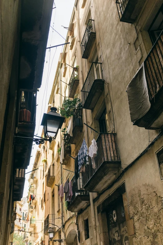 a couple of people walking down a narrow street, inspired by Modest Urgell, unsplash contest winner, balconies, photo of poor condition, things hanging from ceiling, lush