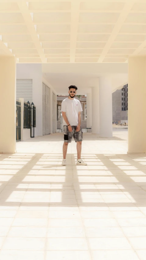 a man standing in the middle of a walkway, an album cover, inspired by Ahmed Yacoubi, pexels contest winner, wearing shorts and t shirt, in white room, in sunny weather, portrait full body