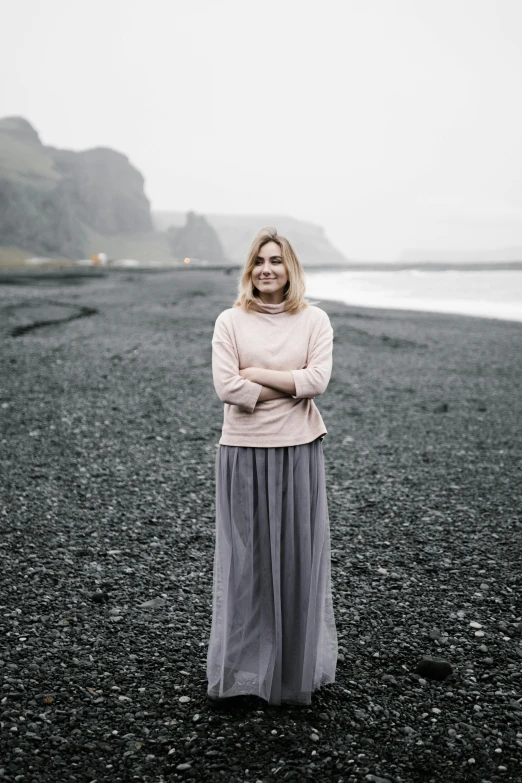 a woman standing on a beach next to the ocean, inspired by Nína Tryggvadóttir, renaissance, grey sweater, pink, forest setting in iceland, high-quality photo