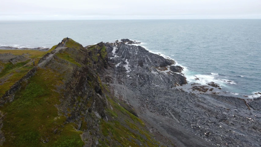 a man standing on top of a cliff next to the ocean, by Þórarinn B. Þorláksson, hurufiyya, rail tracks lead from the mine, photo taken in 2018, natural stone road, seen from a distance