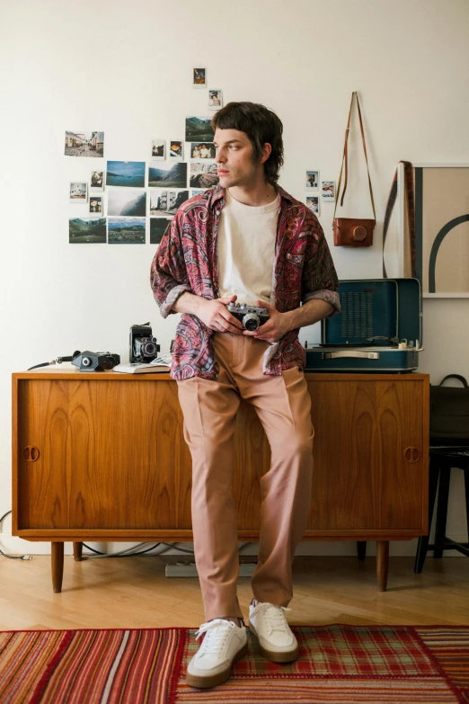 a man standing in a living room holding a camera, inspired by Wes Anderson, renaissance, wearing pants, multi chromatic, standing on a desk, shot with sony alpha