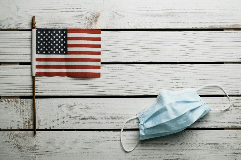 a face mask next to an american flag, a picture, shutterstock, on a wooden table, rectangle, white finish, healthcare