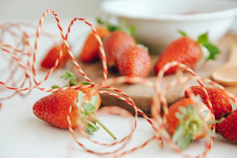 a bunch of strawberries sitting on top of a cutting board, by Sylvia Wishart, pexels contest winner, orange ribbons, strings, on a white table, romantic lead