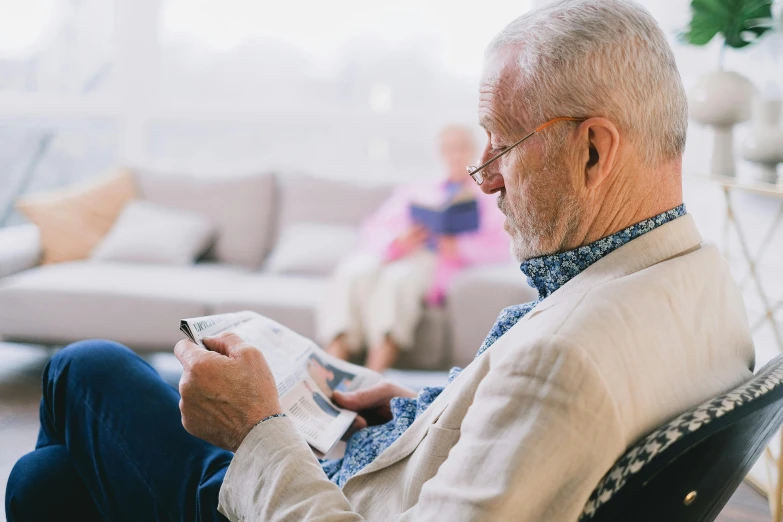 a man sitting in a chair reading a book, a photo, by Will Ellis, pexels contest winner, private press, local conspirologist, sitting on couch, profile image, two old people