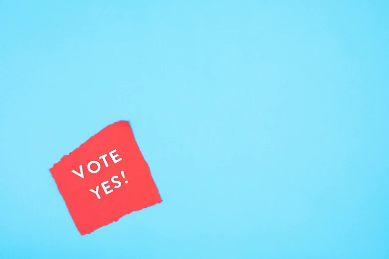 a red piece of paper with the word vote yes on it, shutterstock contest winner, visual art, relaxed. blue background, canva, aerial shot, lgbtq