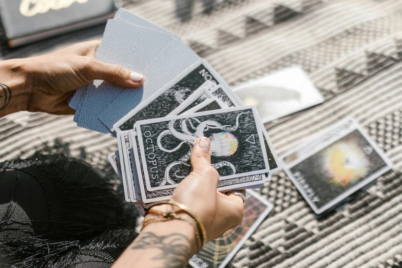 a woman sitting on a bed holding a deck of cards, by Julia Pishtar, pexels contest winner, holographic artifacts, on a sunny day, doing witchcraft, close-up shot from behind