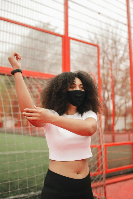 a woman standing in front of a soccer goal wearing a face mask, pexels, renaissance, black bandage on arms, photo of a black woman, stretch, wearing a cropped tops