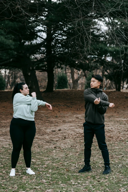 a couple of people that are standing in the grass, choreographed, at a park, non-binary, preparing to fight