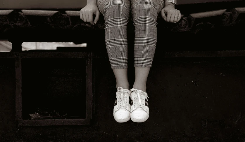 a black and white photo of a person sitting on a bed, inspired by Vivian Maier, pexels contest winner, realism, wearing white sneakers, plaid tights, sit on a bench, mixed media photography