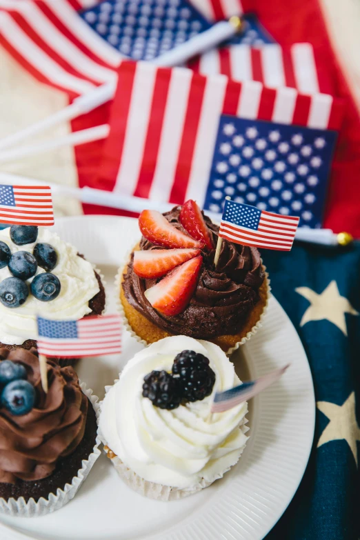 a white plate topped with cupcakes covered in frosting, pexels, american realism, navy flags, fruit, us, gold