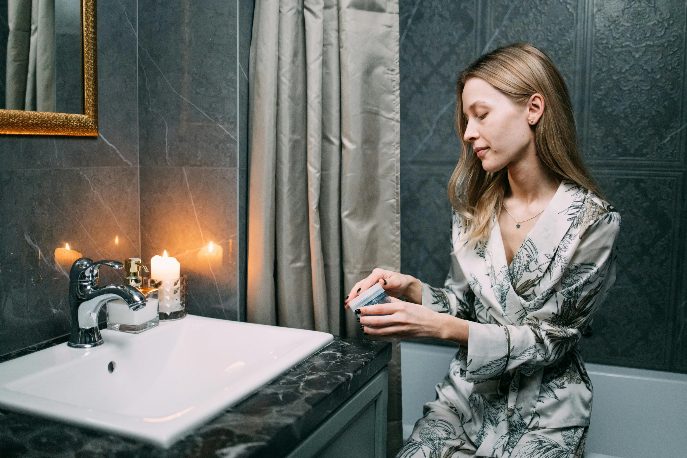 a woman sitting in a bath room next to a sink, by Julia Pishtar, trending on pexels, renaissance, wearing a grey robe, holding a candle holder, someone sits in bed, profile image