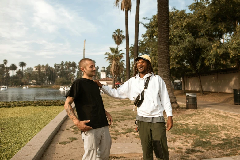 two men standing next to each other on a sidewalk, a photo, wiz khalifa, in a city park, riverside, interview