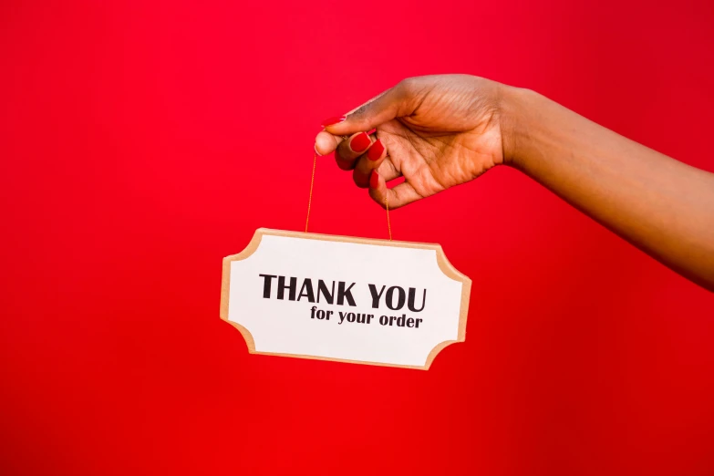 a person holding a sign that says thank you for your delivery, by Julia Pishtar, pexels contest winner, in red background, essence, detailed product shot, malika favre
