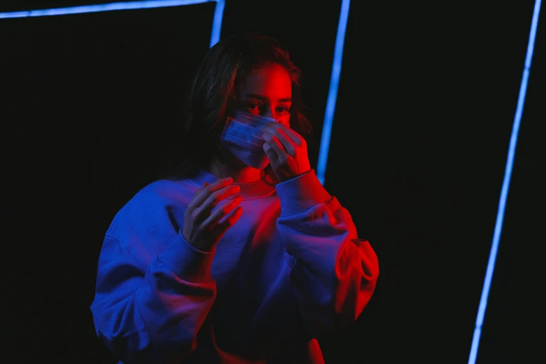 a woman standing in front of a neon light, inspired by Elsa Bleda, pexels contest winner, holography, surgical mask covering mouth, teenage girl, red and blue black light, coughing