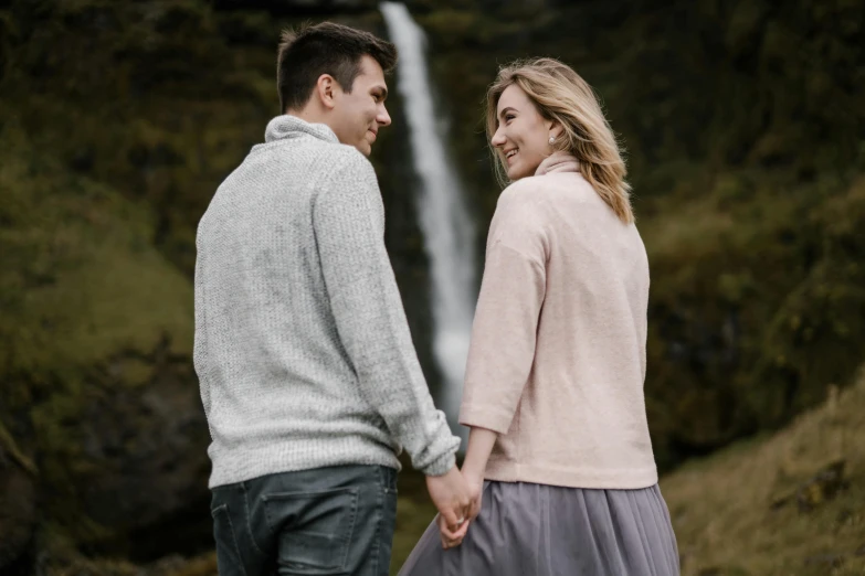 a man and woman holding hands in front of a waterfall, by Hallsteinn Sigurðsson, pexels contest winner, renaissance, flirting smiling, gray, lightly dressed, promotional image