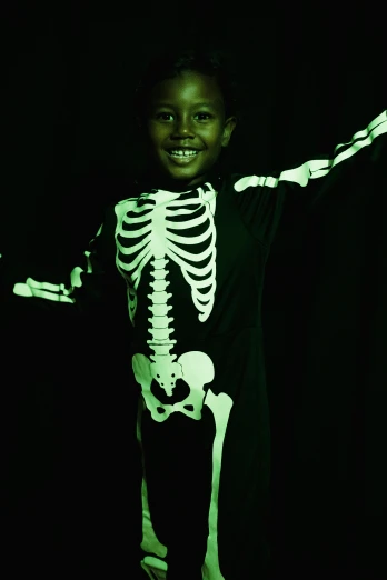 a young boy dressed up in a skeleton costume, by Ruth Abrahams, pexels, process art, glow in dark, ( ( dark skin ) ), vantablack gi, press shot