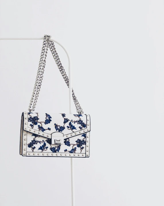 a white and blue purse sitting on top of a table, reddit, in front of white back drop, flowery, high resolution product photo, wearing studded leather