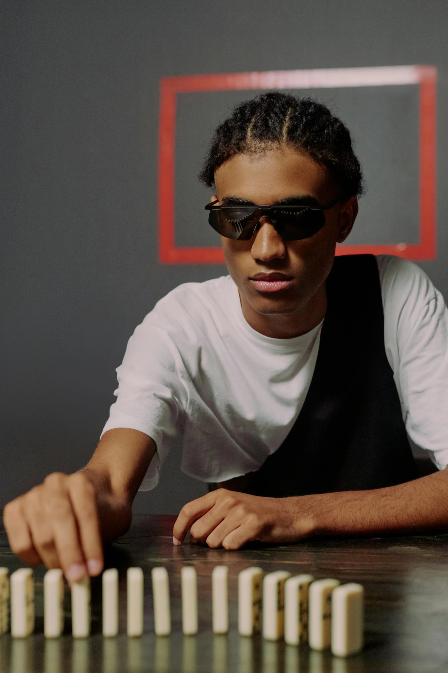 a man sitting at a table with dominos in front of him, an album cover, inspired by Barthélemy Menn, trending on pexels, futuristic sunglasses, black teenage boy, confident pose, with index finger