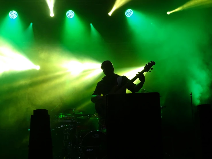 a man that is playing a guitar on a stage, ambient green light, profile pic, backscatter orbs, low quality photo