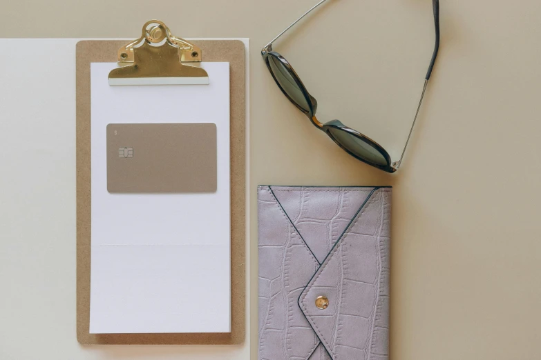 a pair of sunglasses and a clipboard on a table, by Emma Andijewska, trending on pexels, minimalism, taupe, business card, gold and purple, with two front pockets