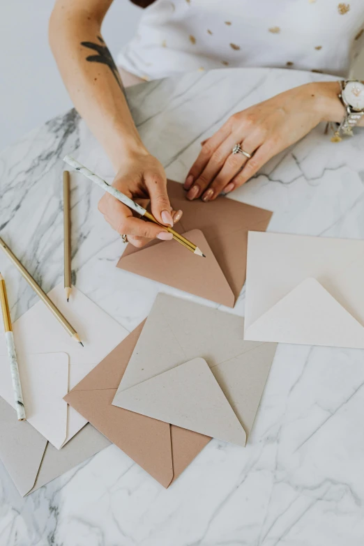 a woman sitting at a table working on a piece of paper, featured on instagram, private press, beige and gold tones, greeting card, thumbnail, square shapes