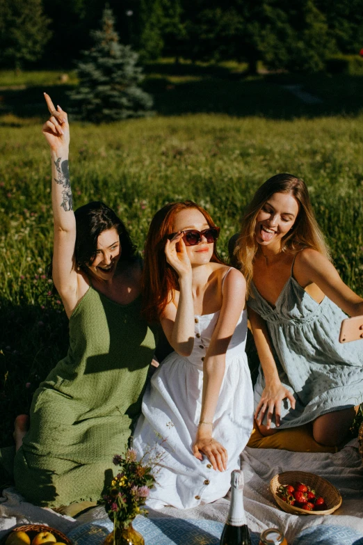 a group of women sitting on top of a grass covered field, with sunglass, portrait featured on unsplash, sundress, playful pose