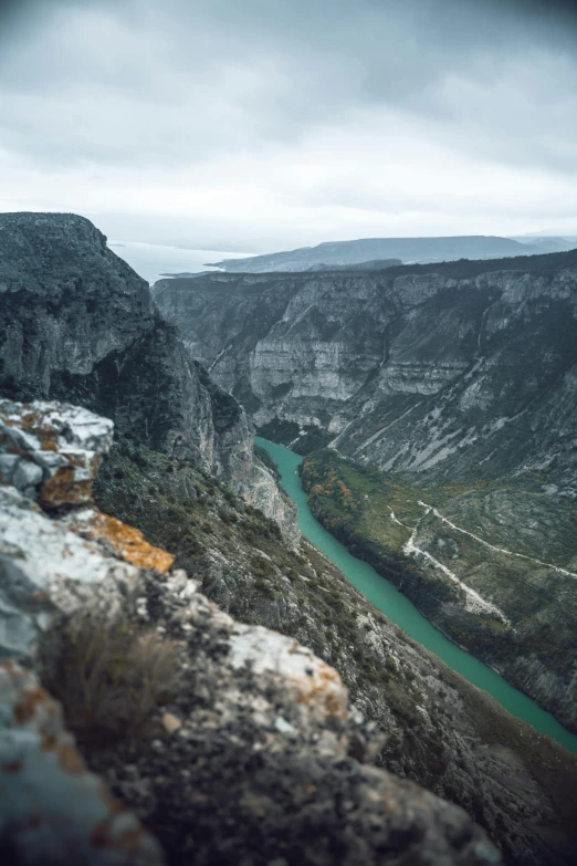 a man standing on top of a cliff next to a river, greece, photo of green river, square, ominous and intense