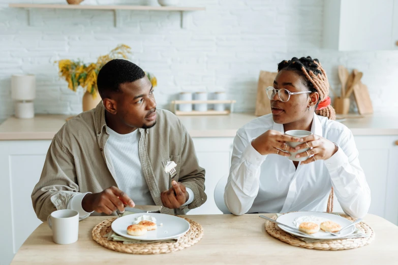 two people sitting at a table with plates of food, a portrait, trending on pexels, brown, morning coffee, looking at each other mindlessly, wearing medium - sized glasses