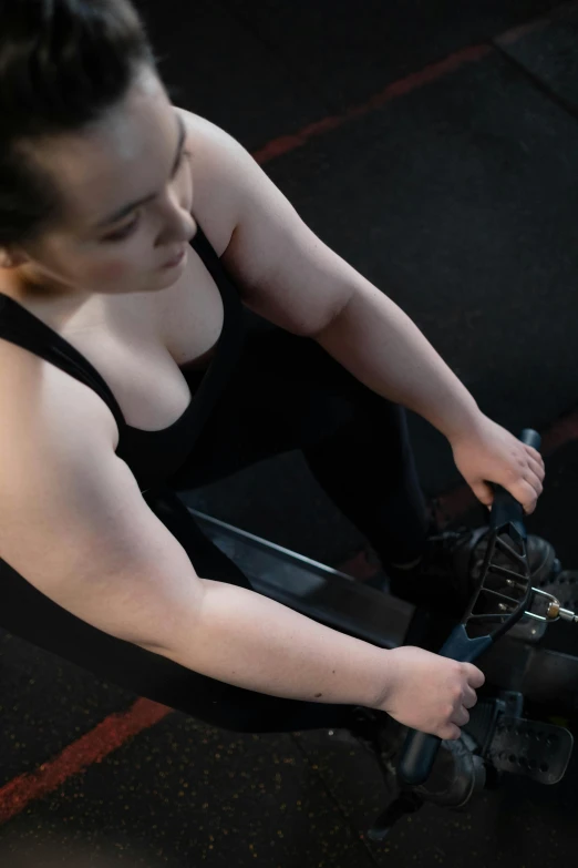 a woman sitting on the ground holding a video game controller, inspired by Louisa Matthíasdóttir, pexels contest winner, curvy crossfit build, on the bow, dingy gym, low quality photo