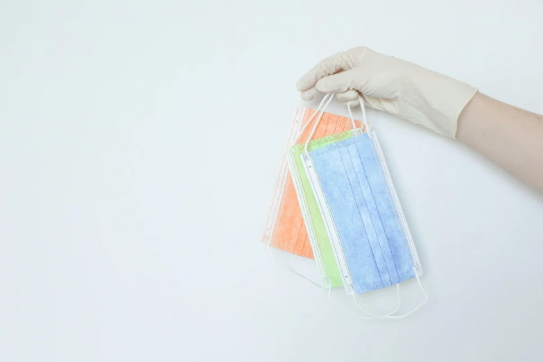 a person holding a bunch of surgical masks, pexels, sōsaku hanga, chartreuse and orange and cyan, with a white background, rectangle, three colors