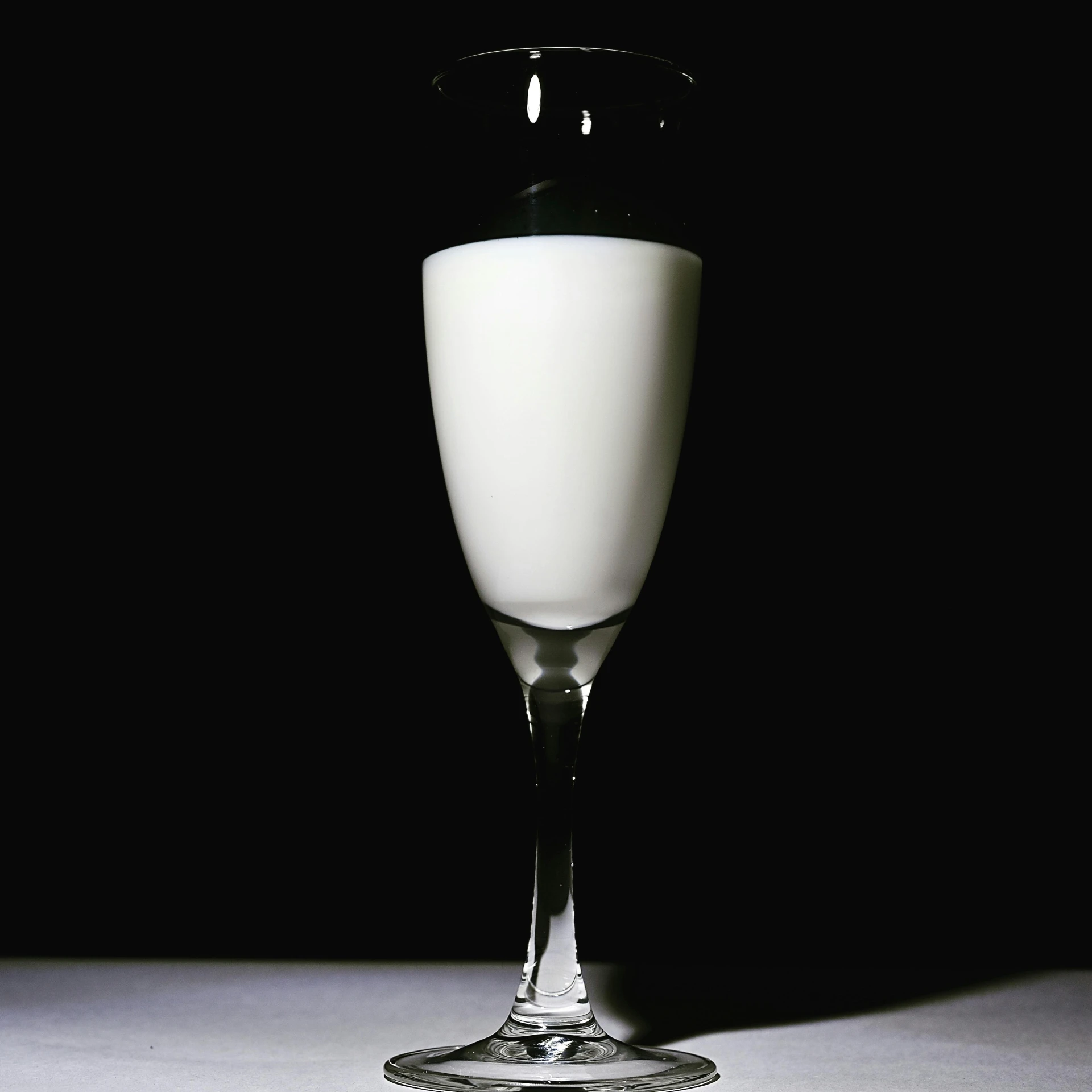 a glass of milk sitting on top of a table, standing with a black background, victoriana, bubbly, with white skin