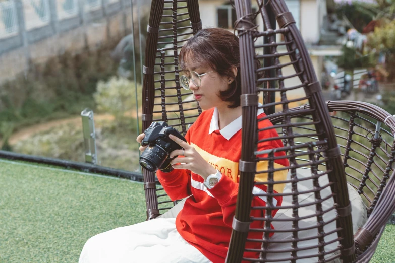 a woman sitting in a chair holding a camera, a picture, inspired by Kim Jeong-hui, pexels contest winner, wearing a scarlet hoodie, 🦩🪐🐞👩🏻🦳, ulzzang, (eos 5ds r