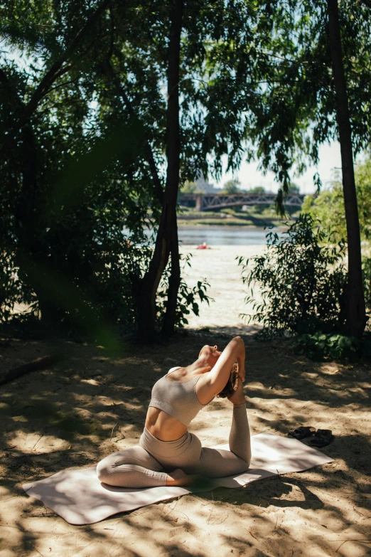 a woman doing a yoga pose on a beach, unsplash, arabesque, with trees and rivers, sunny day in a park, anna nikonova, low quality photo