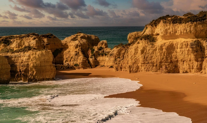 a sandy beach next to the ocean under a cloudy sky, pexels contest winner, renaissance, steep cliffs, rocha, warm glow, thumbnail